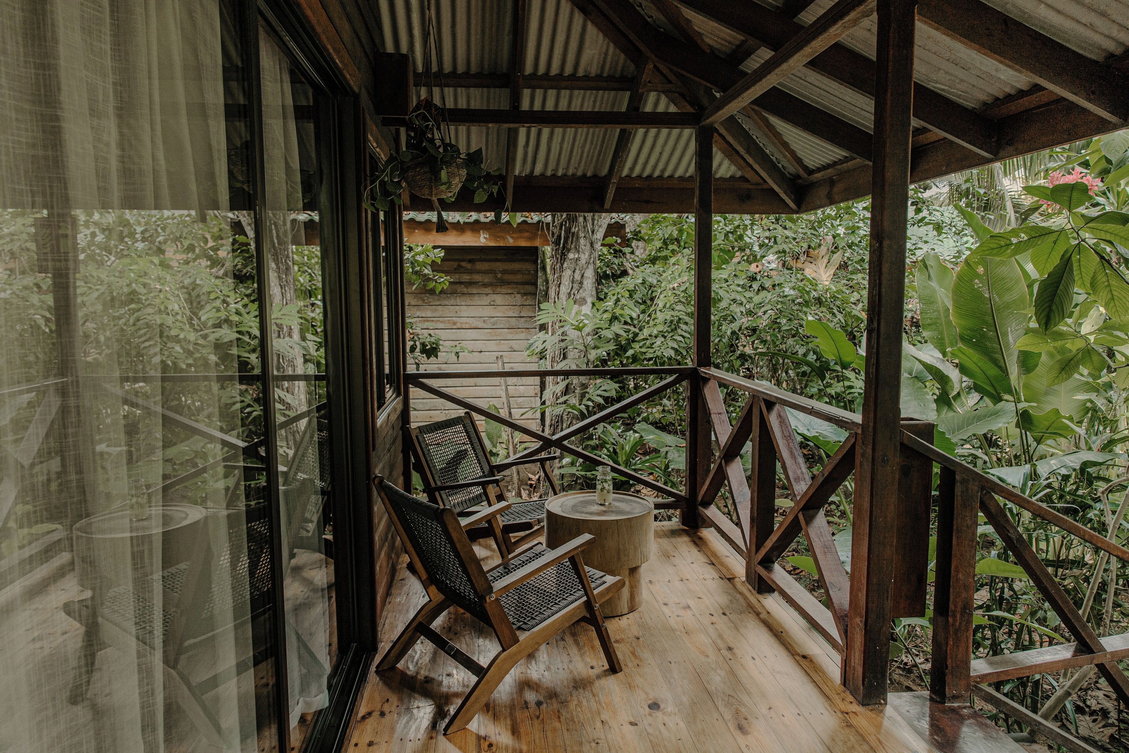 Une terrasse en bois, agrémentée de chaises et d’une table ronde, entourée d’une végétation luxuriante.