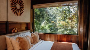 A bedroom with a large window, wooden headboard, and a sunburst wall decoration. - Palmar Beach Lodge (Bastimentos)