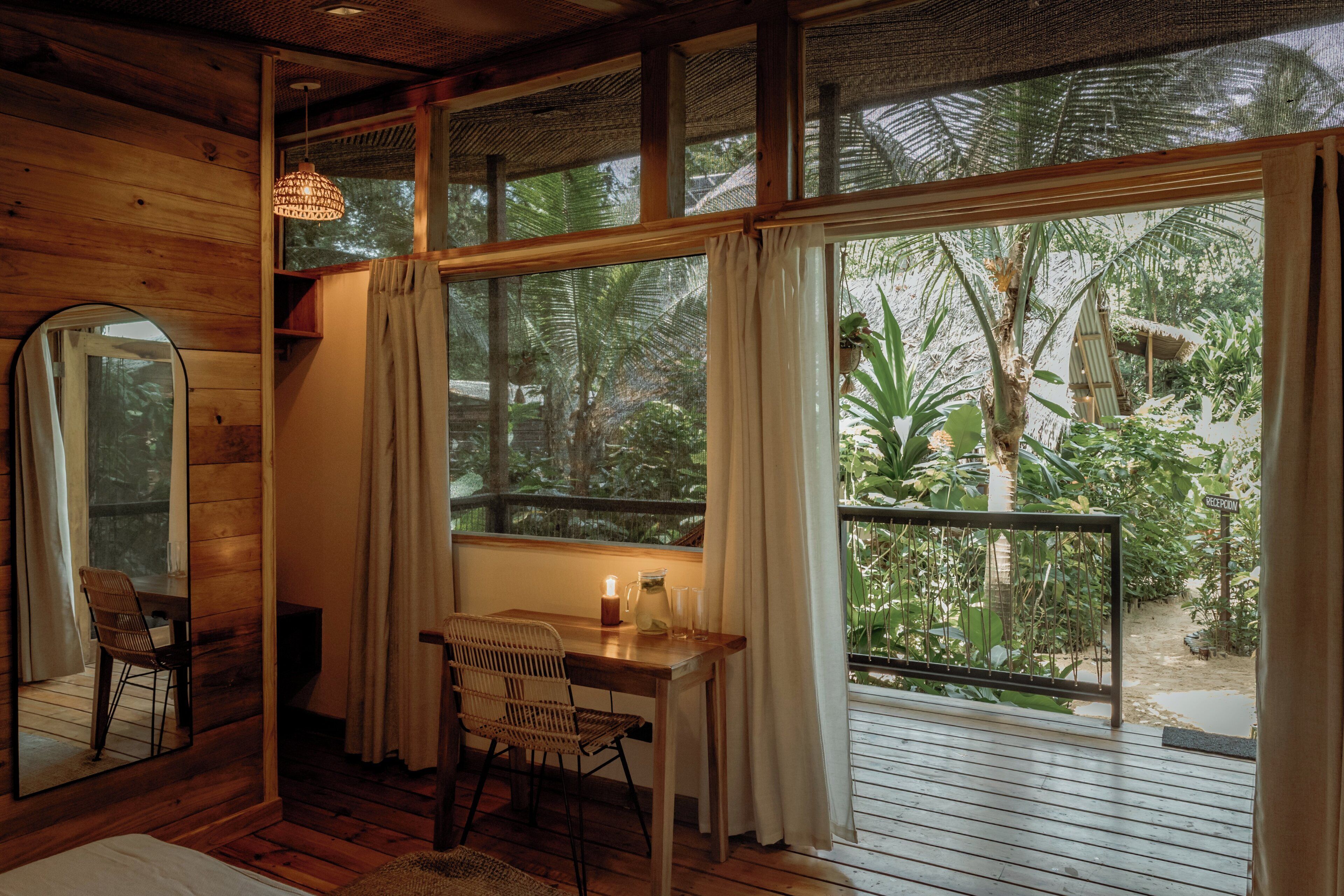 A wooden room with a desk, chair, and a large window overlooking a tropical garden.