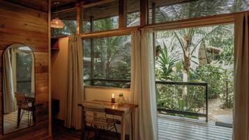 A wooden room with a desk, chair, and a large window overlooking a tropical garden.