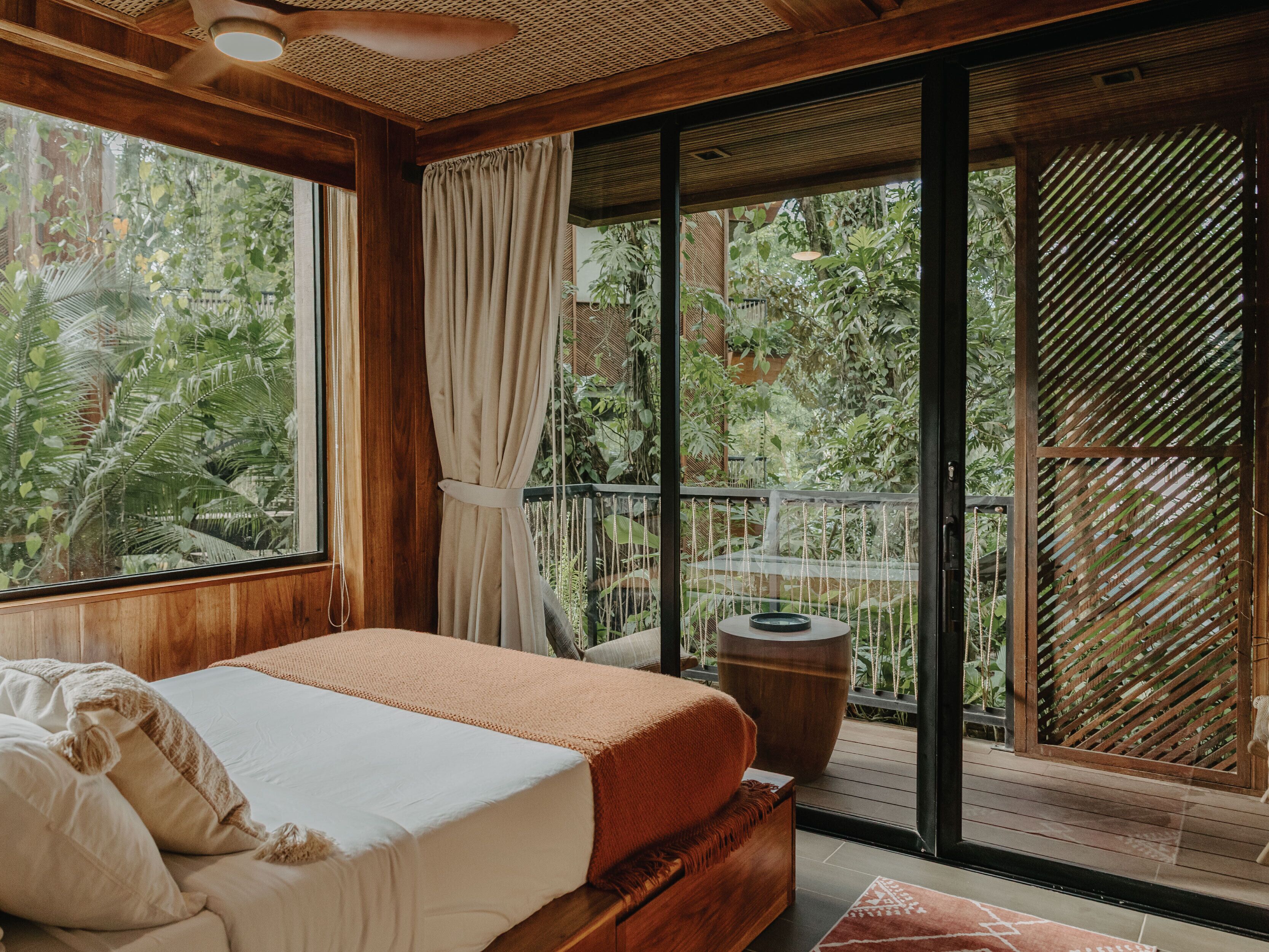 A bedroom with a bed, a wooden headboard, a large window, and a view of greenery outside.