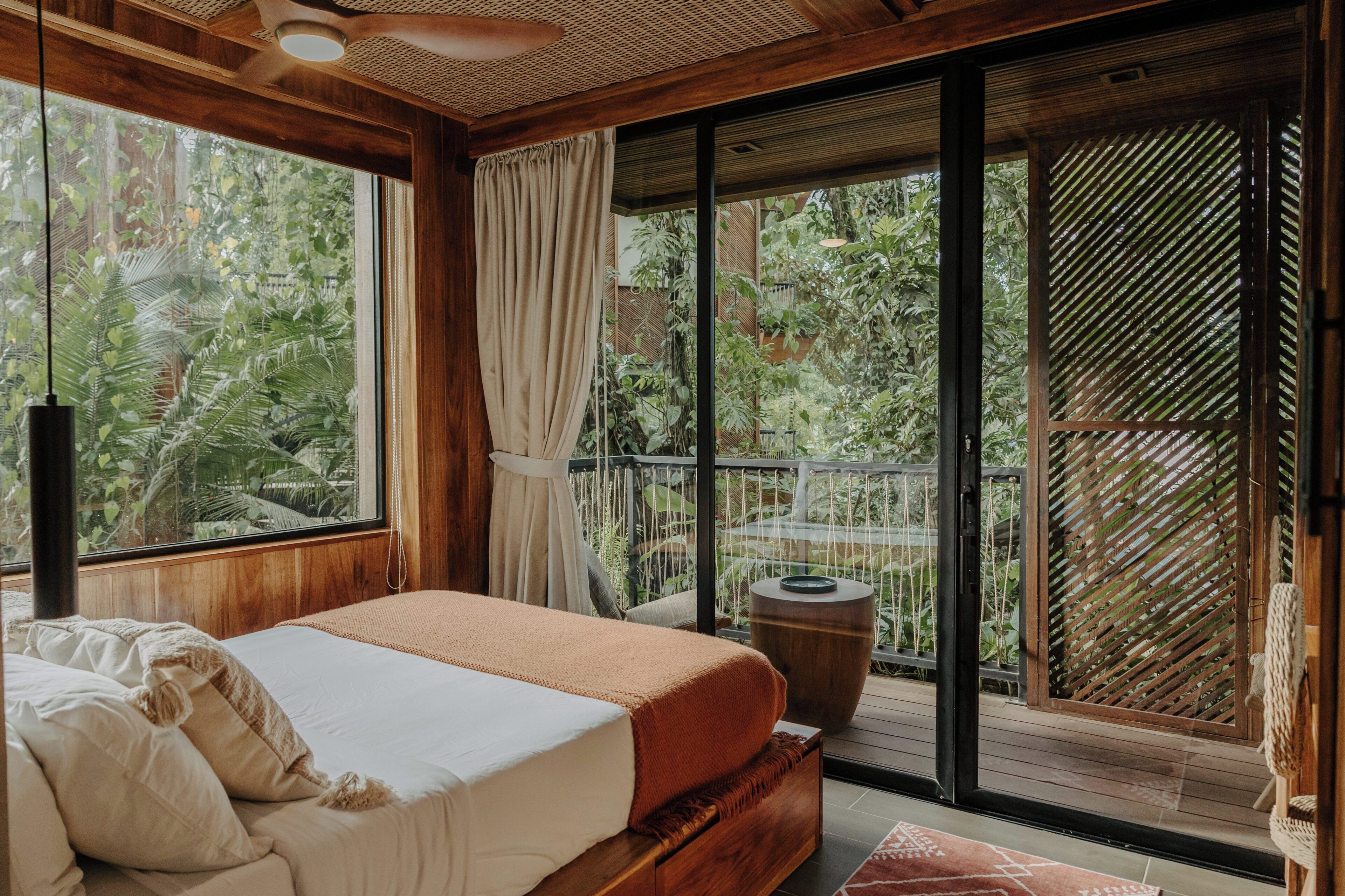 A bedroom with a large bed, a window with curtains, and a view of greenery outside.