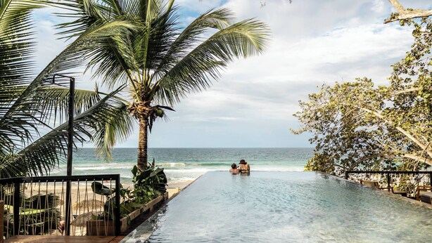A pool with a view of the ocean, palm trees, and a person sitting at the end. - Palmar Beach Lodge (Bastimentos)