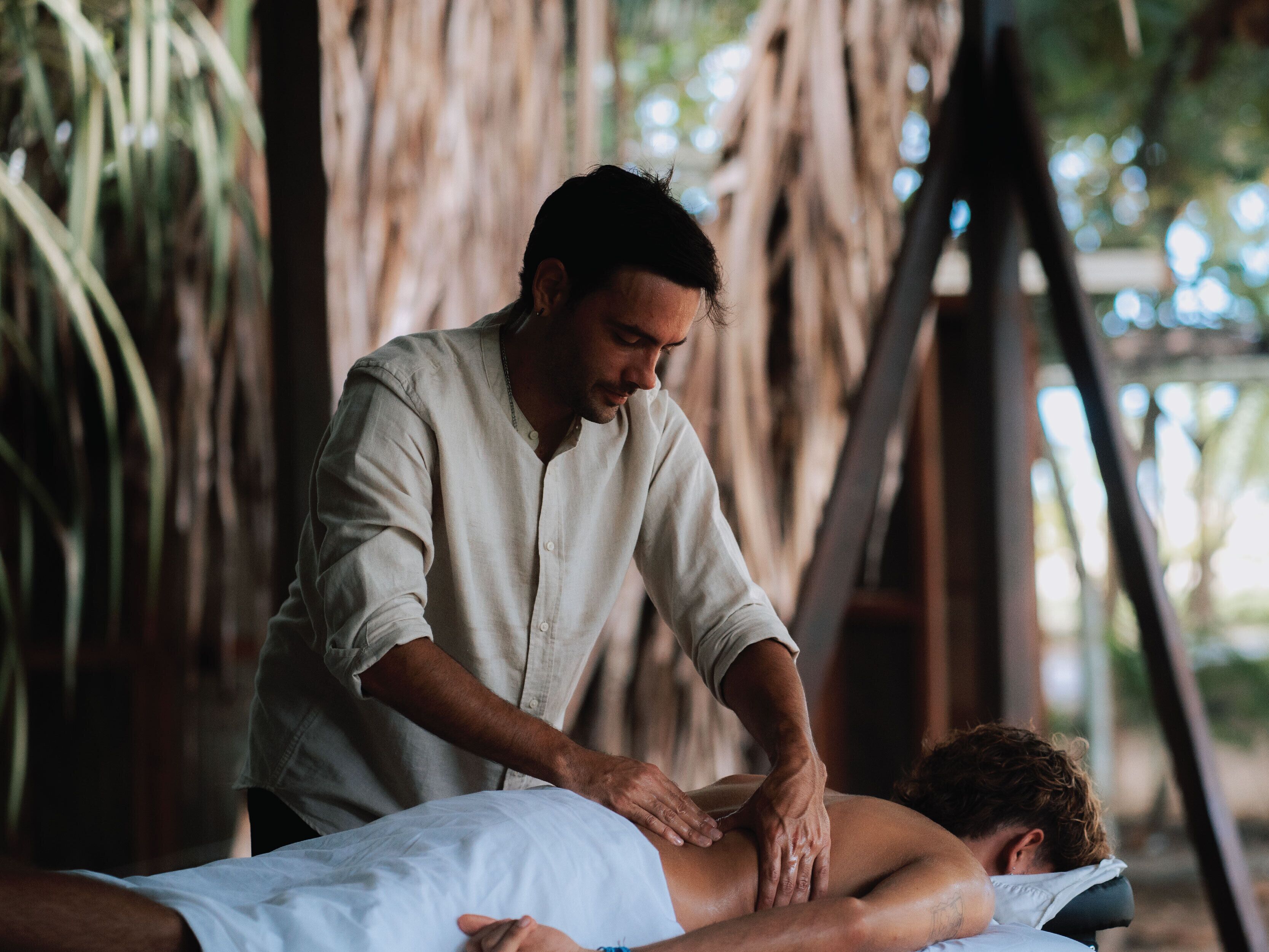 A person receiving a massage in a room with a wooden structure and a view of greenery.