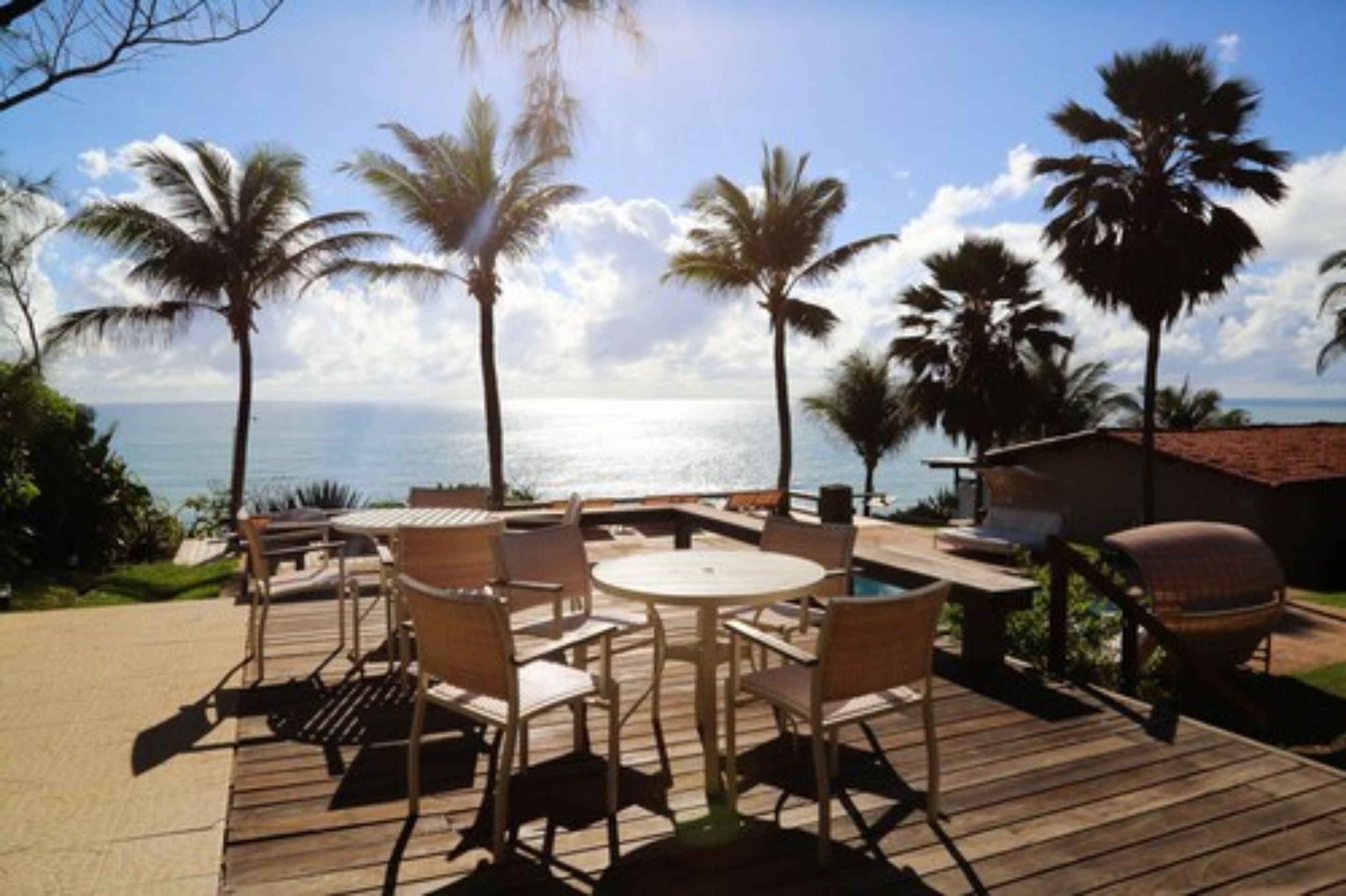Une terrasse en bois avec des meubles d’extérieur, un barbecue et des palmiers donnant sur une étendue d’eau.