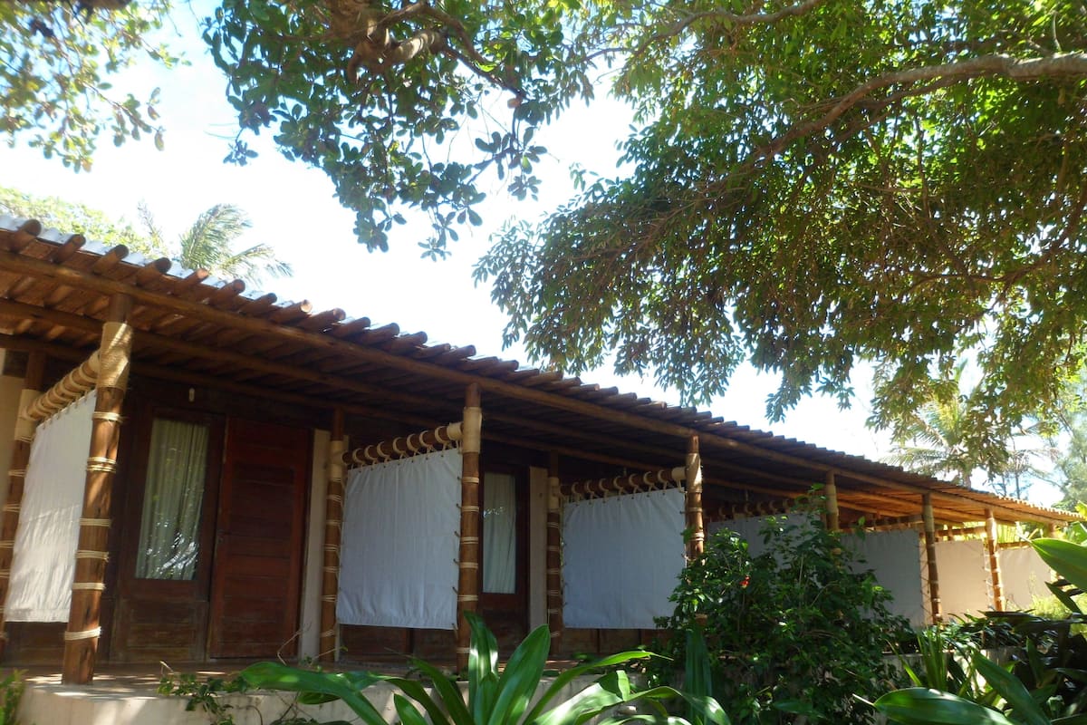 A traditional wooden house with a tiled roof, bamboo pillars, and a covered porch.