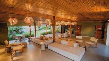 Un espacio interior amplio con techo de madera, varios conjuntos de asientos que incluyen sofás y sillones, y lámparas de mimbre colgantes.