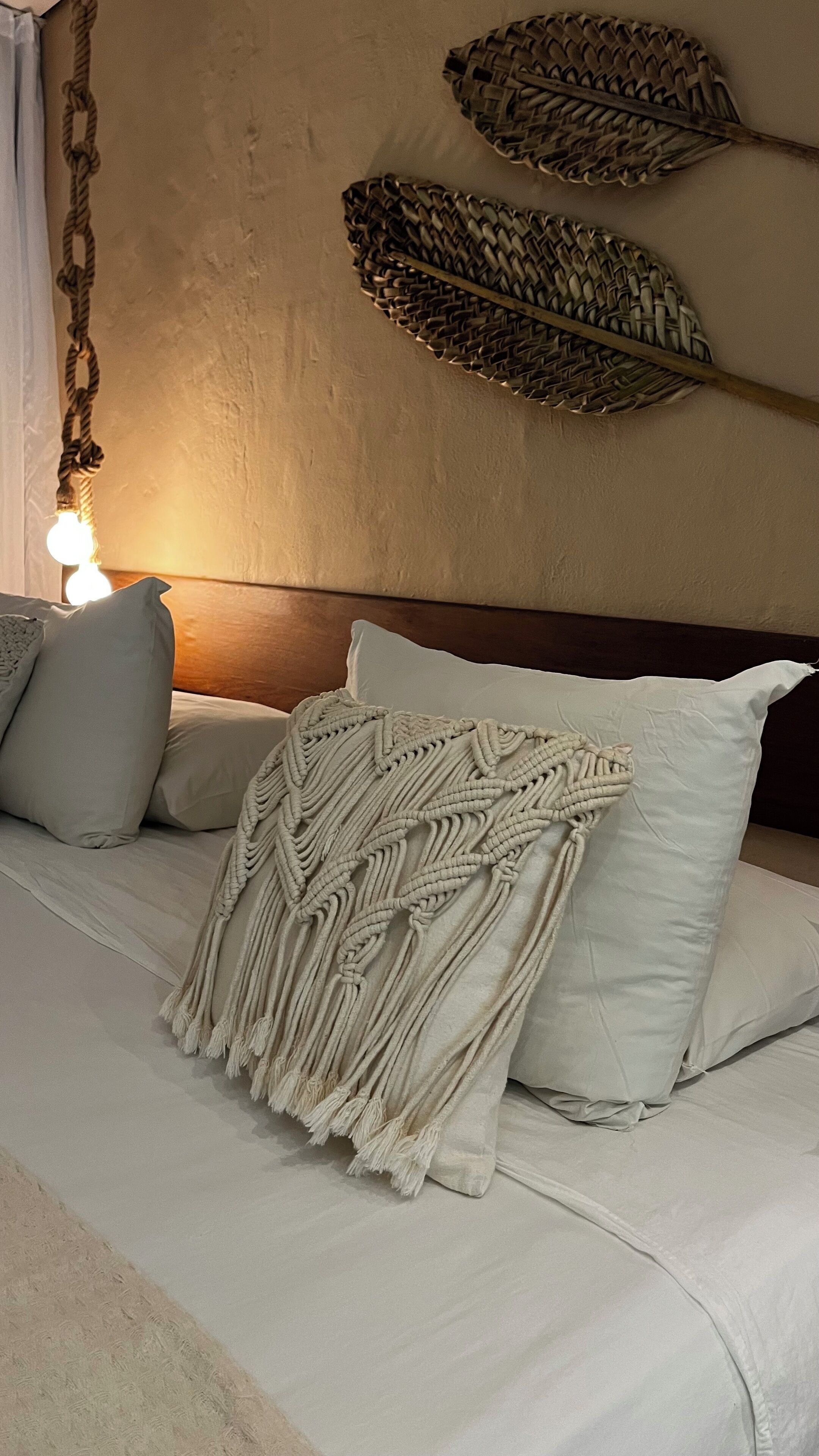 Una cama con una manta de macramé, dos almohadas y un cabecero.