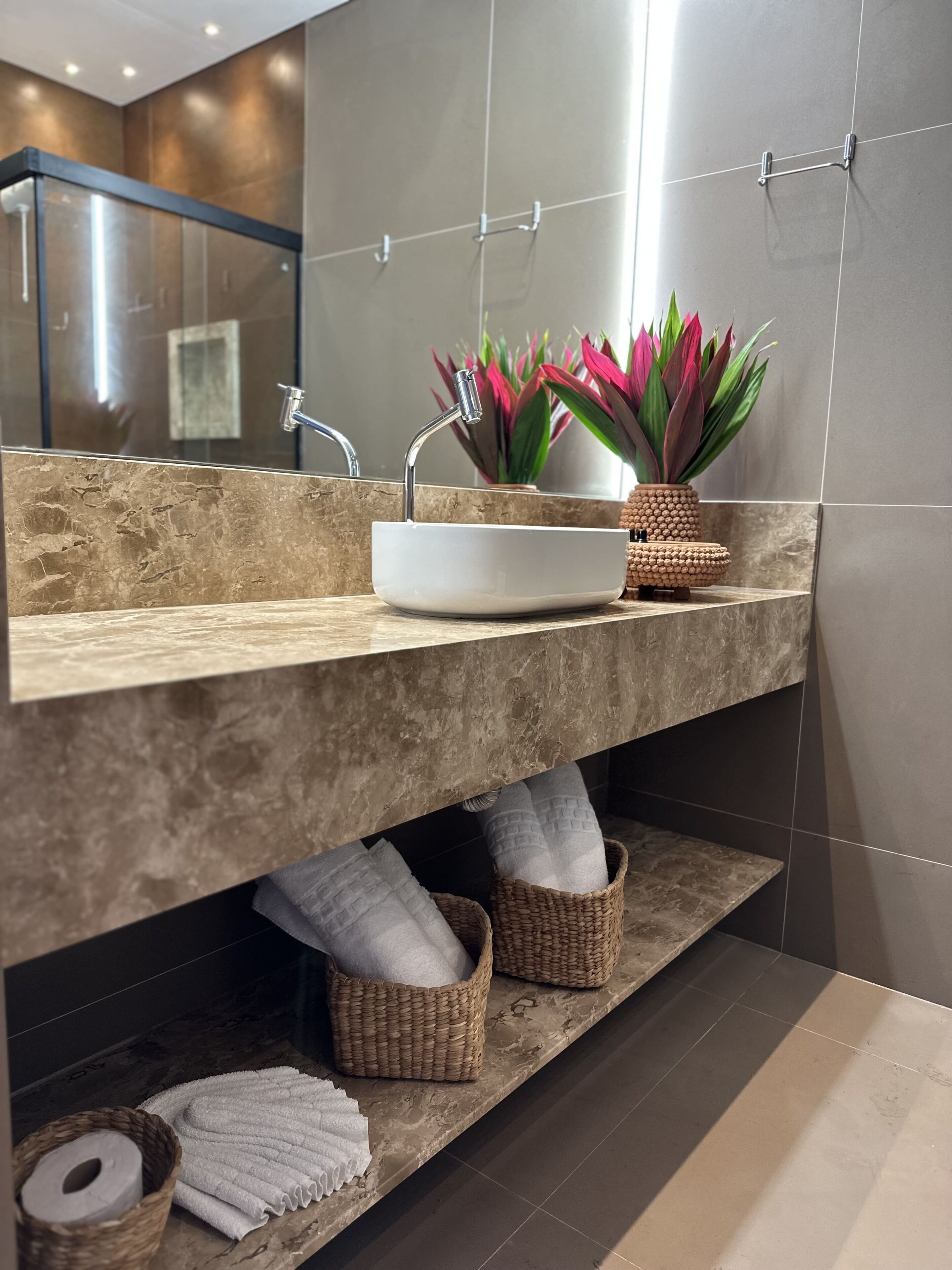 A modern bathroom with a marble countertop, a white sink, a mirror, and a potted plant.