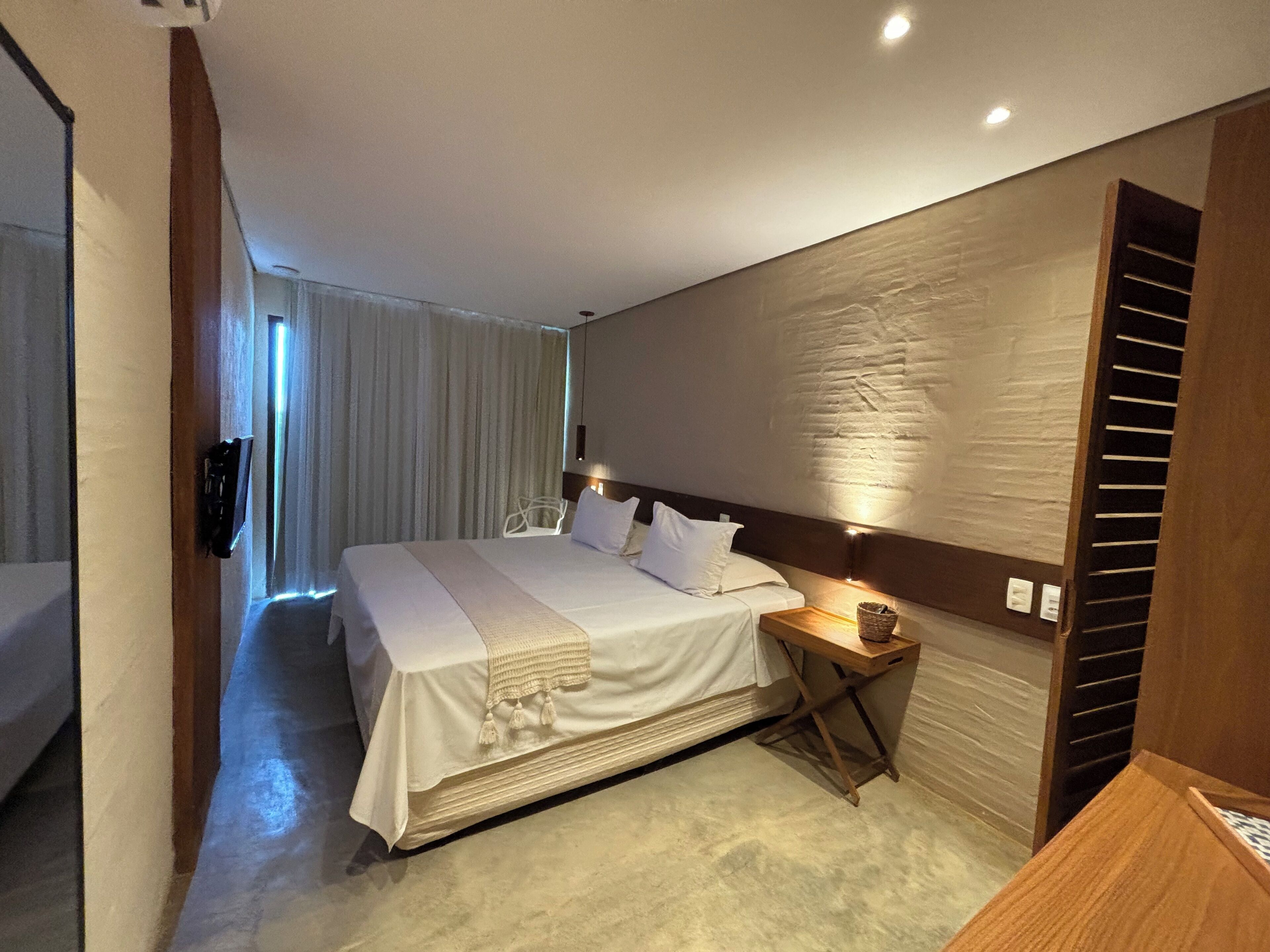 Una habitación de hotel moderna con una cama grande, una mesita de noche y un cabecero de madera.
