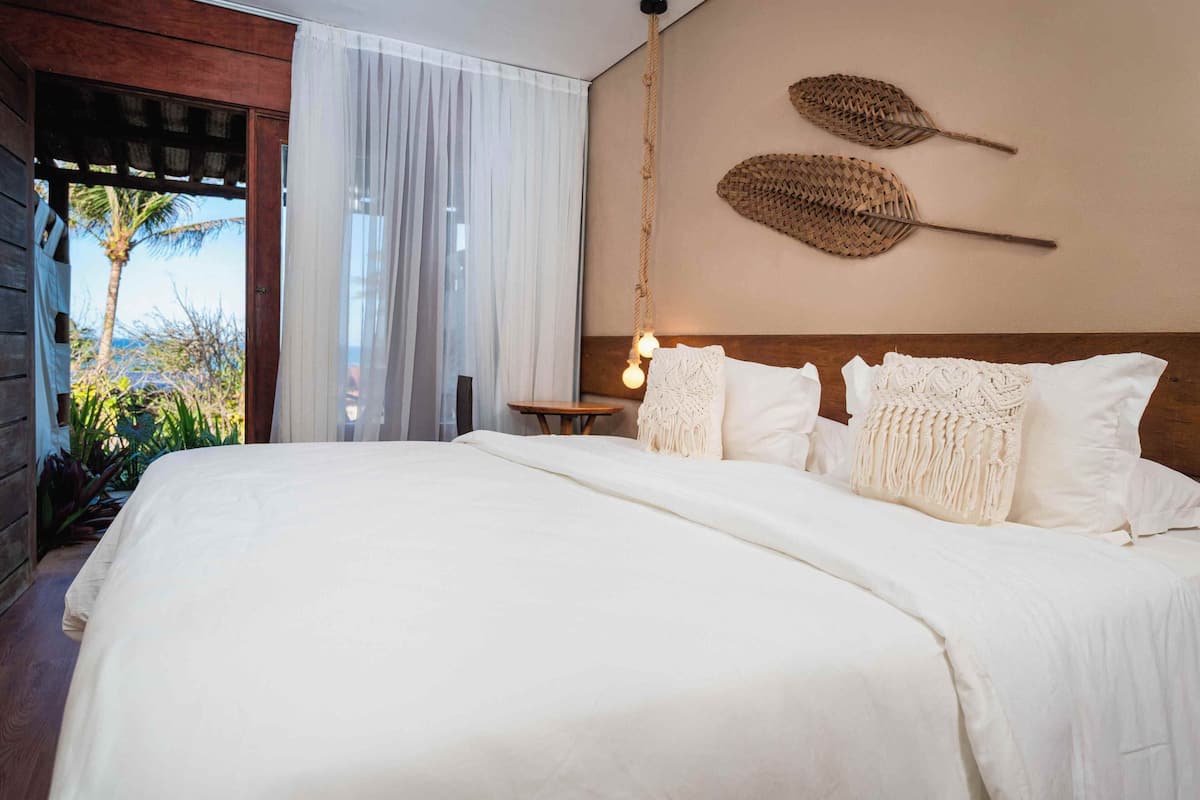 A large bed with white linens, a wooden headboard, and a hanging light fixture.