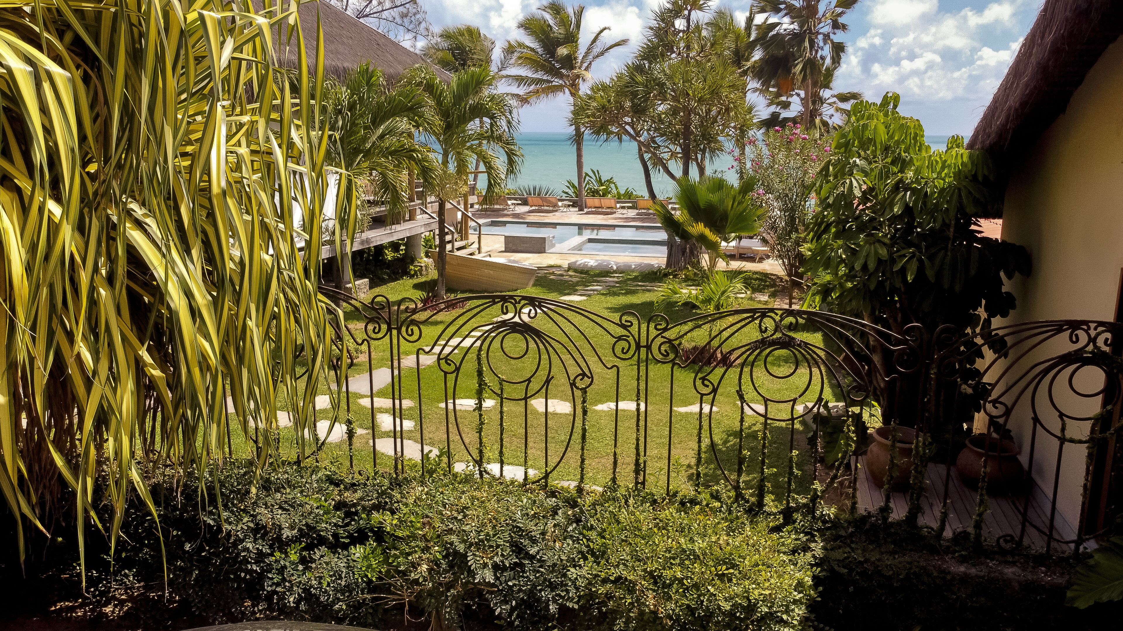 A view of a tropical resort with a pool, palm trees, and a clear view of the ocean.