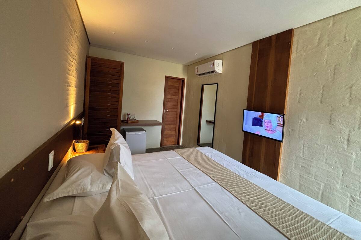 A hotel room with a bed, a small kitchenette, a television, and a mirror.