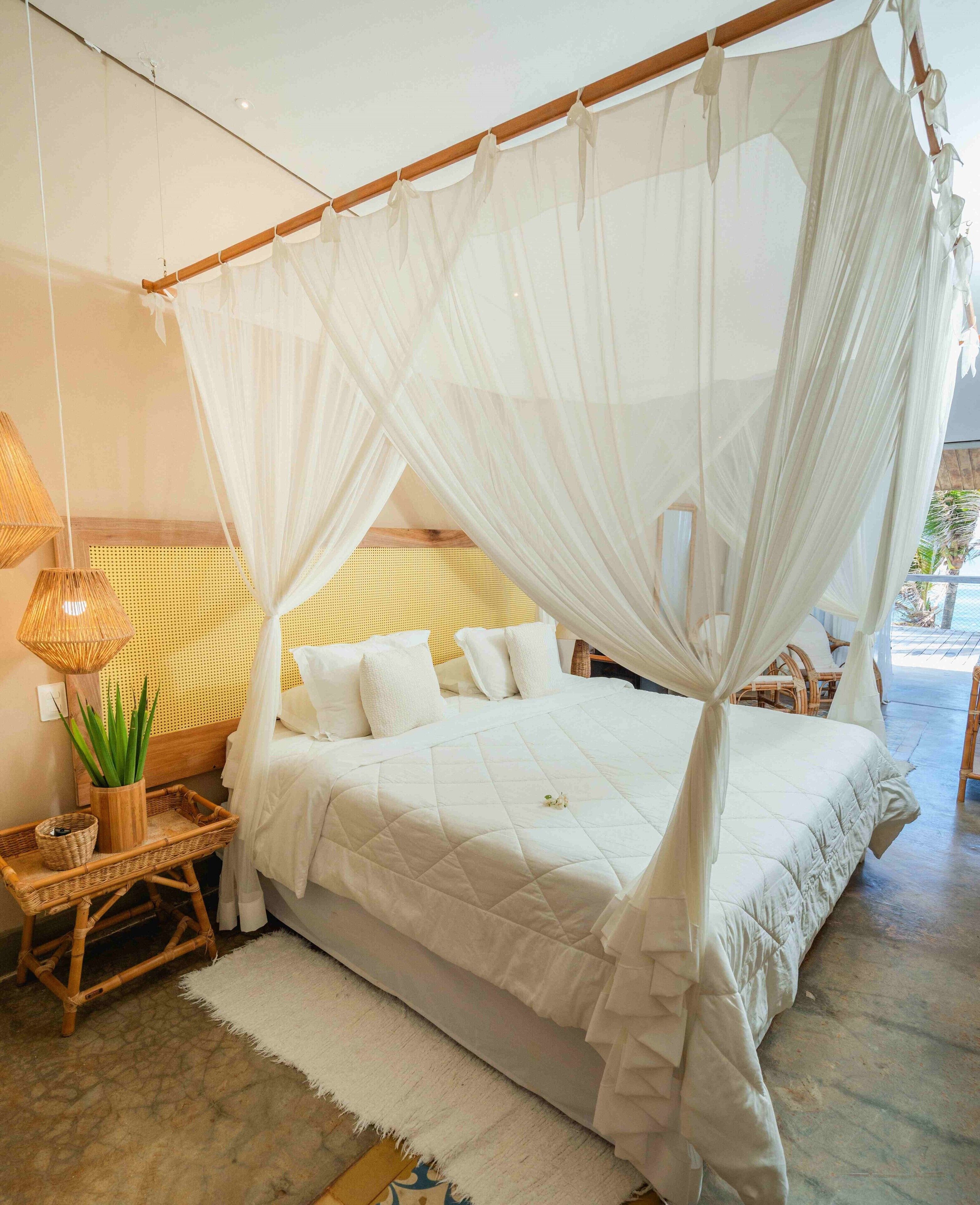 A bed with a canopy, a wicker side table with a plant, and a rattan headboard.