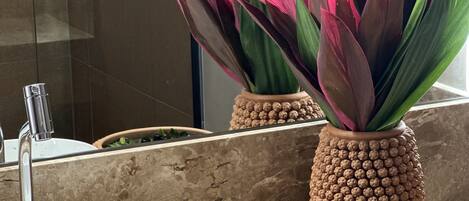 Een badkamer met een wit wastafelmeubel, een spiegel en twee decoratieve potplanten met groene en roze bladeren.