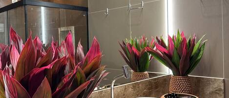 Un baño moderno con un espejo grande, un lavamanos blanco y plantas decorativas en macetas con textura.