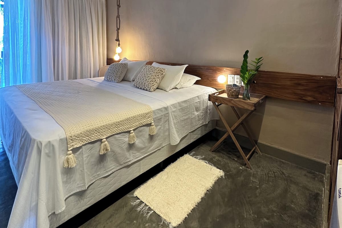A modern bedroom with a large bed, bedside table, and a hanging light fixture.