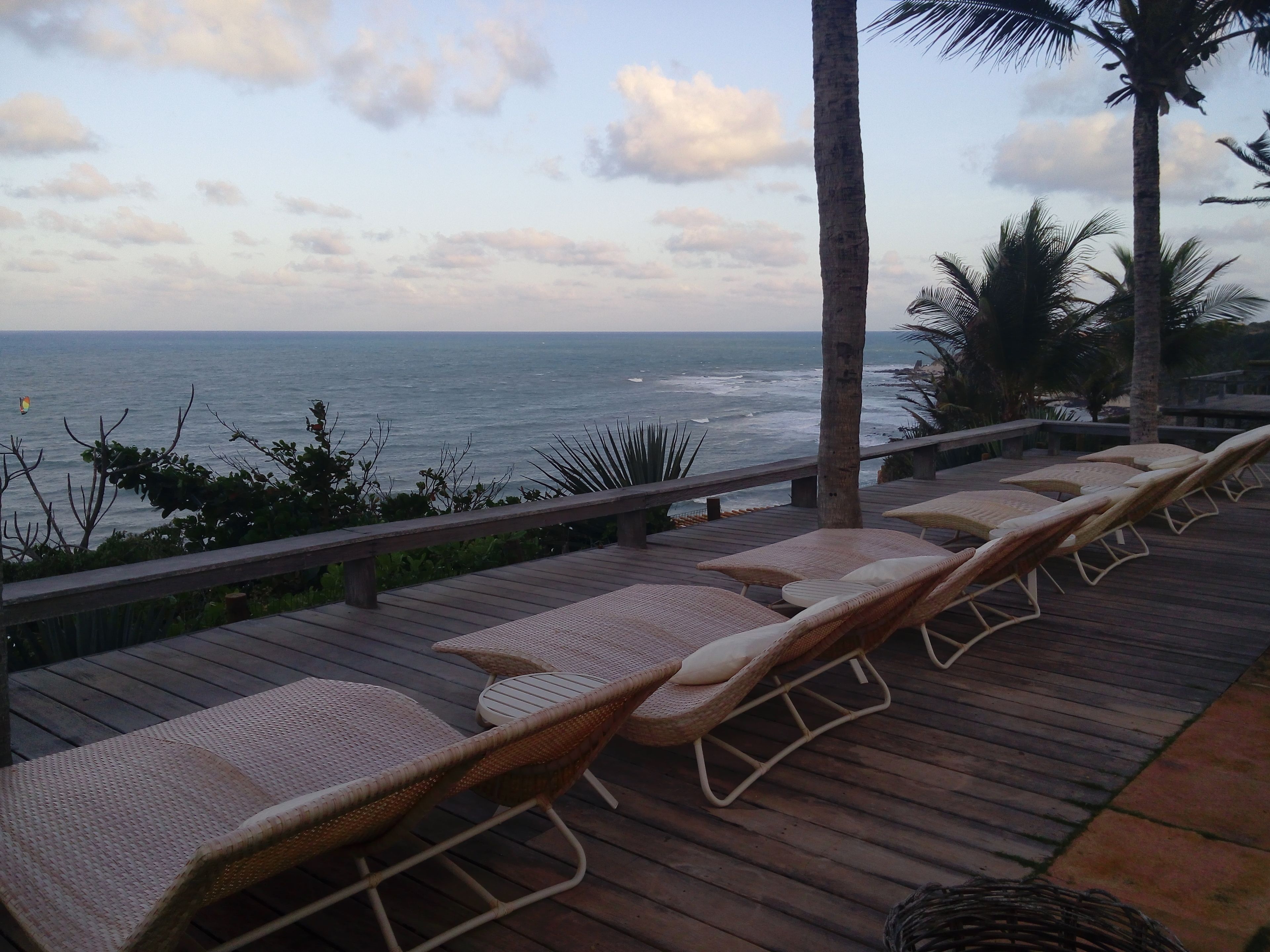 Um deck de madeira com cadeiras de descanso de vime voltado para o oceano.