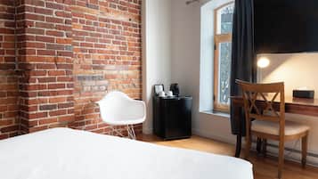 Quarto com parede de tijolos, cama, escrivaninha com cadeira, mesinha e janela com cortinas.