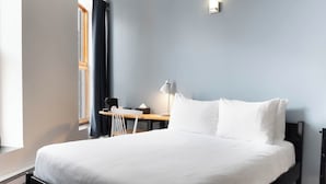 A bedroom with a bed, a desk, a chair, and a window with curtains. - Hotel Belley (Québec City)