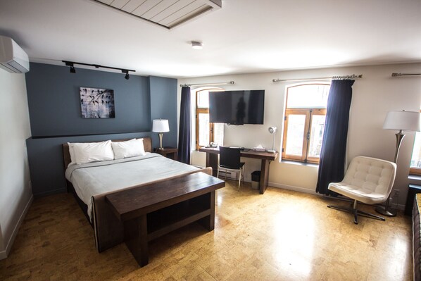 A bedroom with a bed, desk, chair, TV, and artwork.