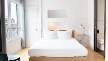Un dormitorio con una cama, una mesita de noche con lámpara, una silla y una ventana.