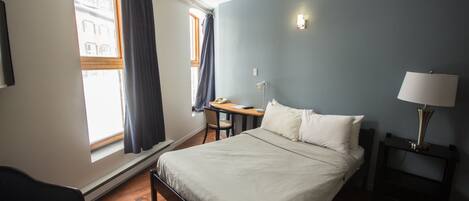A bedroom with a bed, a desk, a chair, a lamp, and a window with curtains.