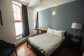 A bedroom with a bed, a desk, a chair, a lamp, and a window with curtains. - Hotel Belley (Québec City)