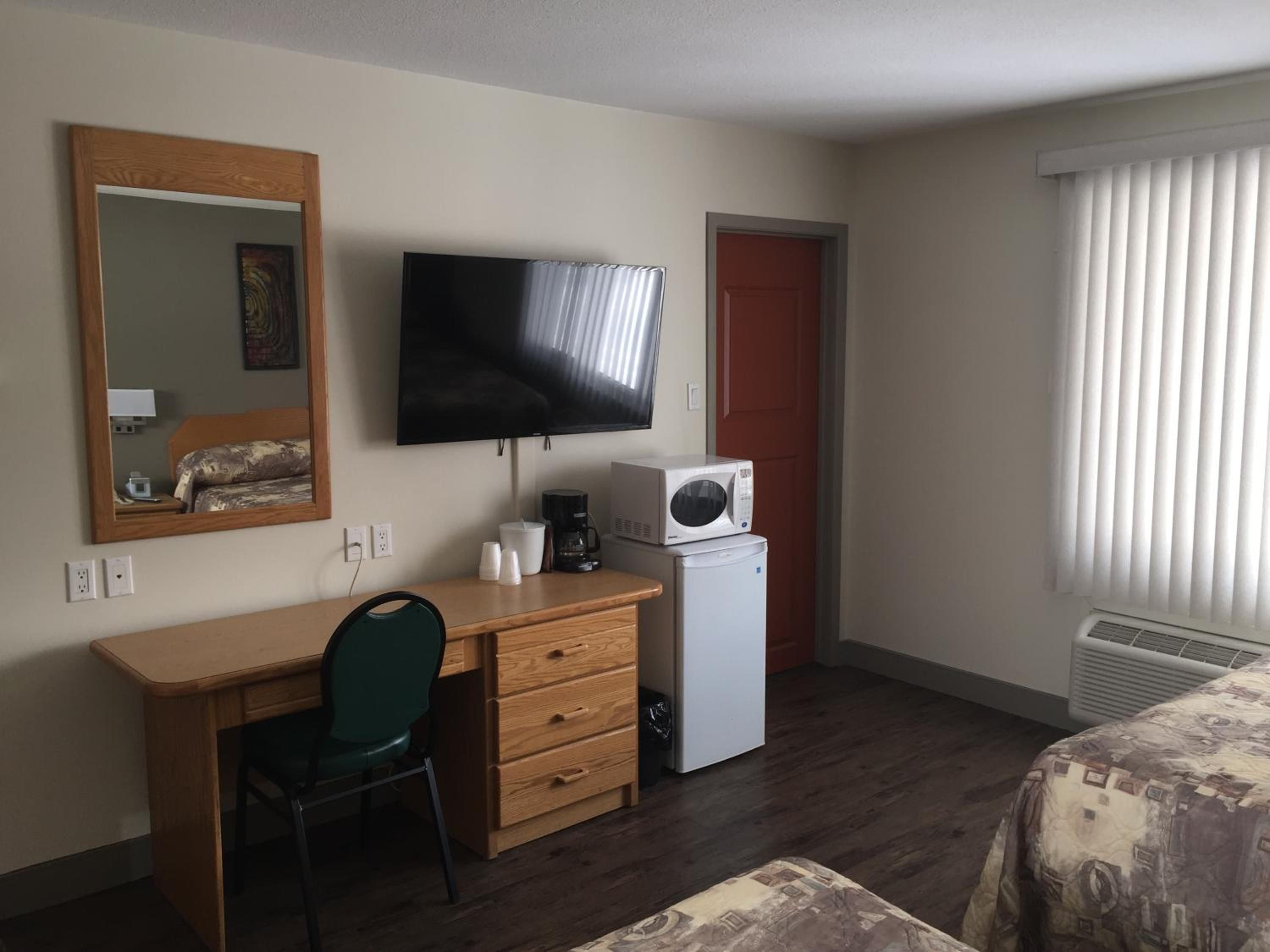 Habitación de hotel con escritorio de madera, televisión, microondas, cafetera, silla y cama.