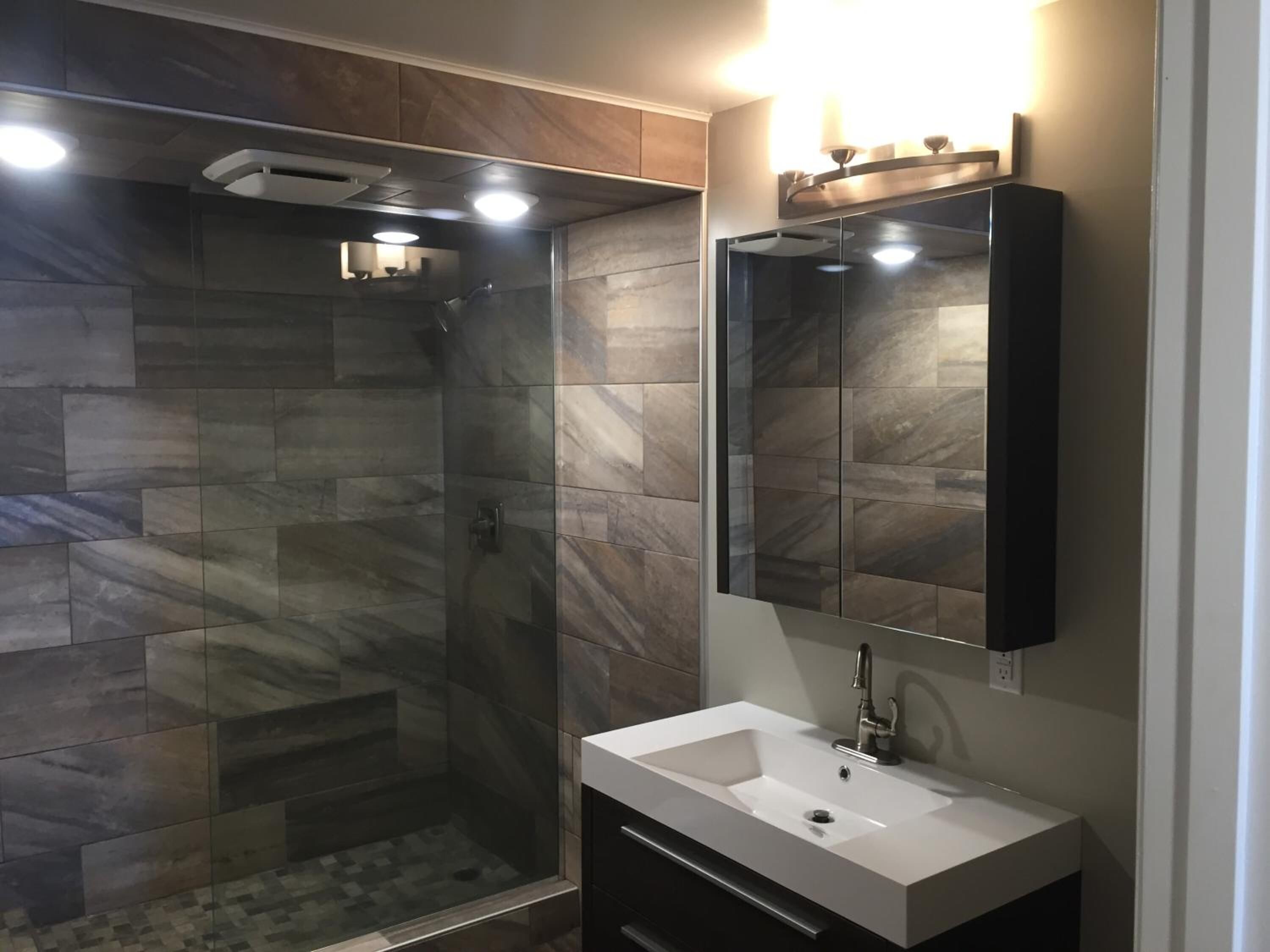 A modern bathroom with a glass-enclosed shower, a white sink, and a large mirror.