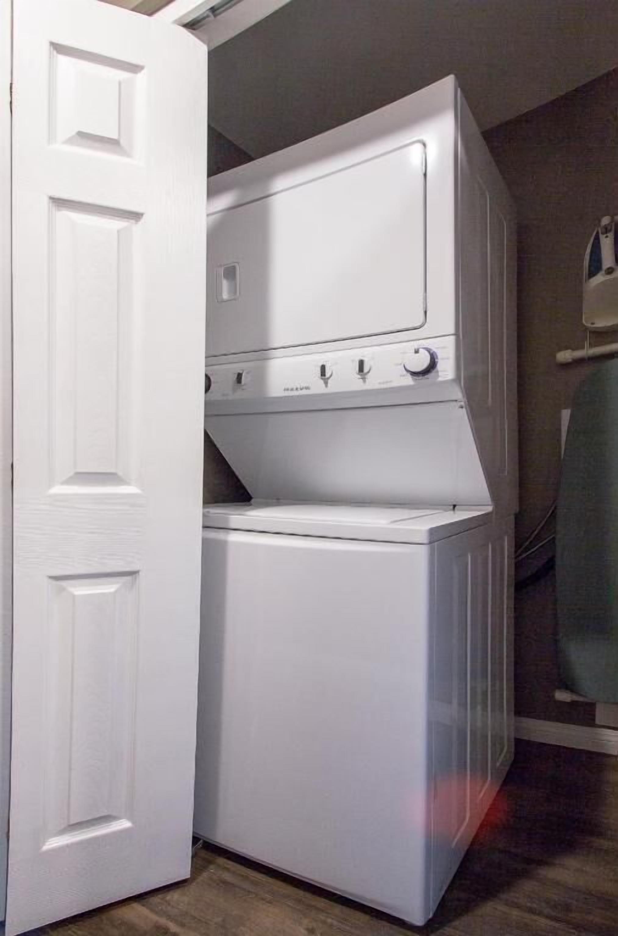 A compact laundry room with a stacked washer and dryer, a door, and a towel rack.