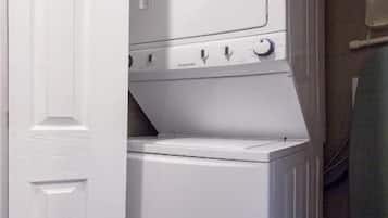 A compact laundry room with a stacked washer and dryer, a door, and a towel rack.