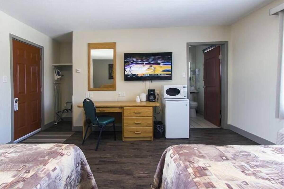 Hotellihuone, jossa on kaksi sänkyä, työpöytä tuolilla, televisio, mikroaaltouuni ja pieni vaatekaappi.