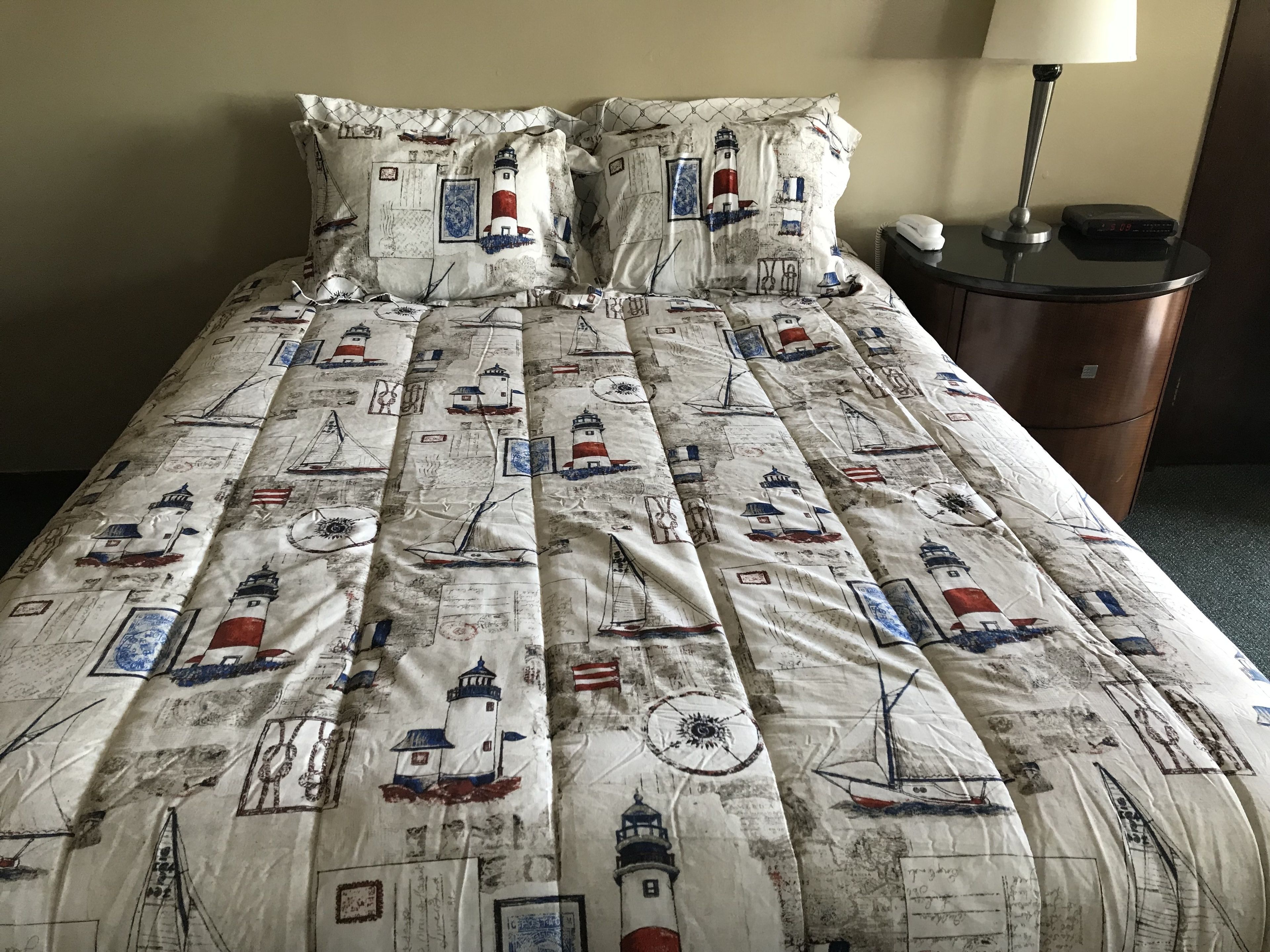 A bed with a nautical-themed duvet cover featuring lighthouses and ships.