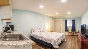 A compact hotel room with a bed, a desk, a chair, a TV, a sink, and a window with curtains.