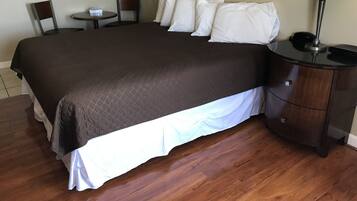 A neatly made bed with a dark quilt, a bedside table with a lamp, and a small round table with a chair.
