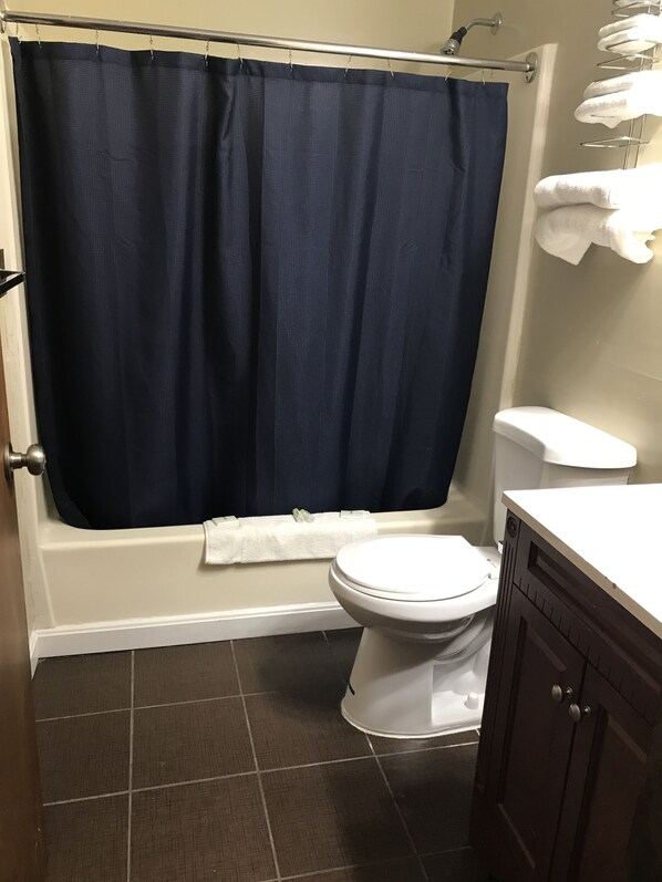 A bathroom with a bathtub, toilet, and dark brown tiled floor.