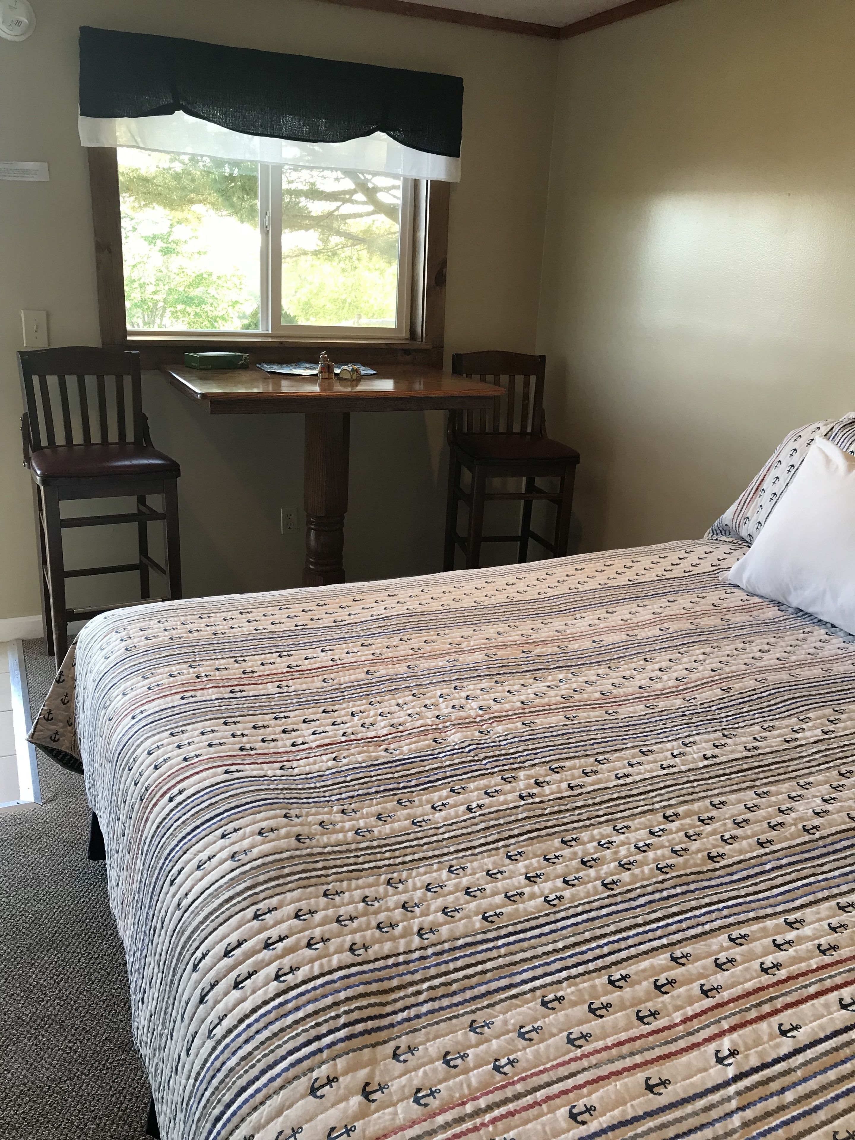 Une chambre à coucher comprenant un lit, deux chaises, une petite table et une fenêtre donnant sur un paysage verdoyant.