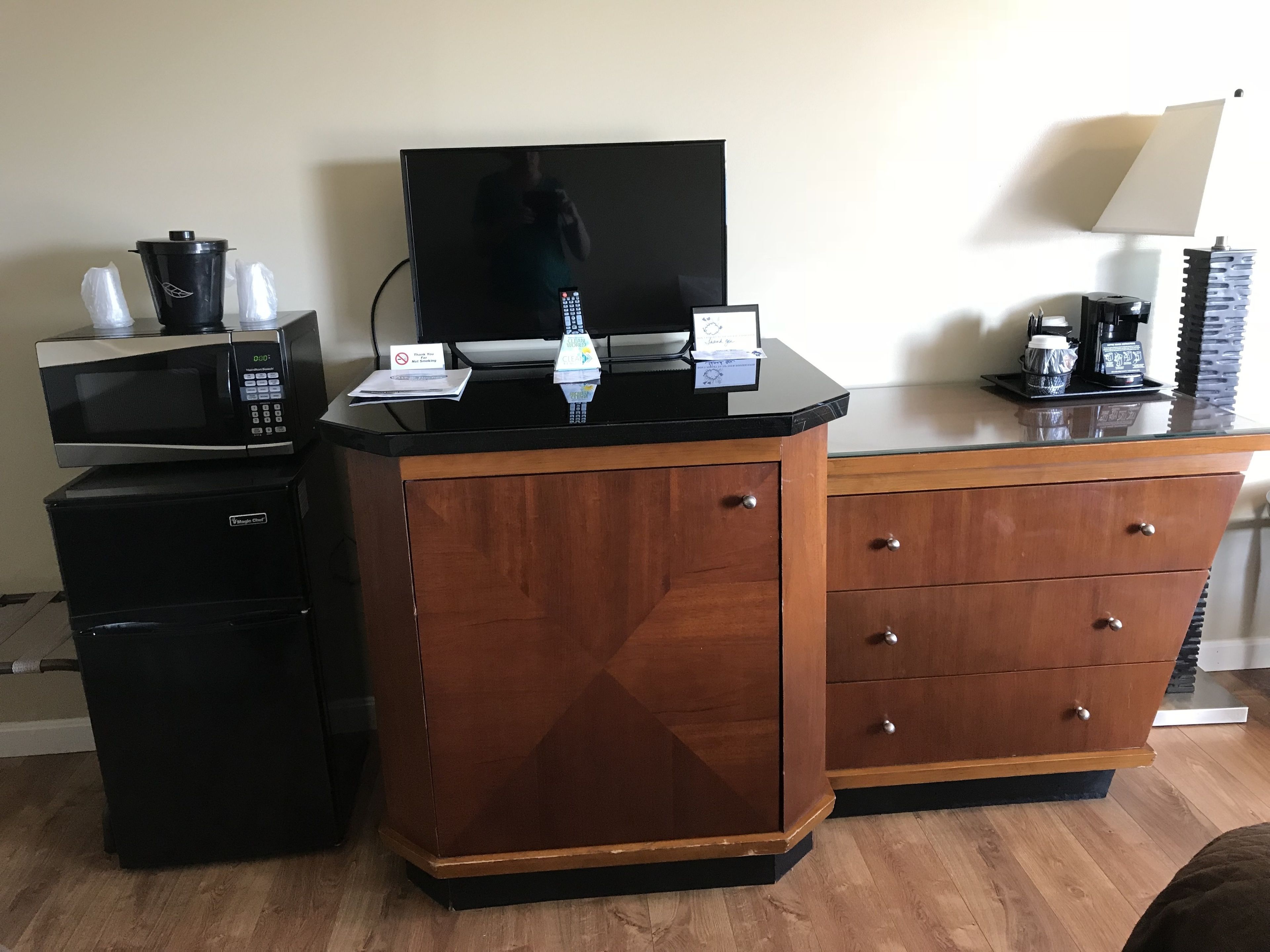 Una camera d'albergo con un armadietto in legno, un forno a microonde, una macchina da caffè e un televisore.