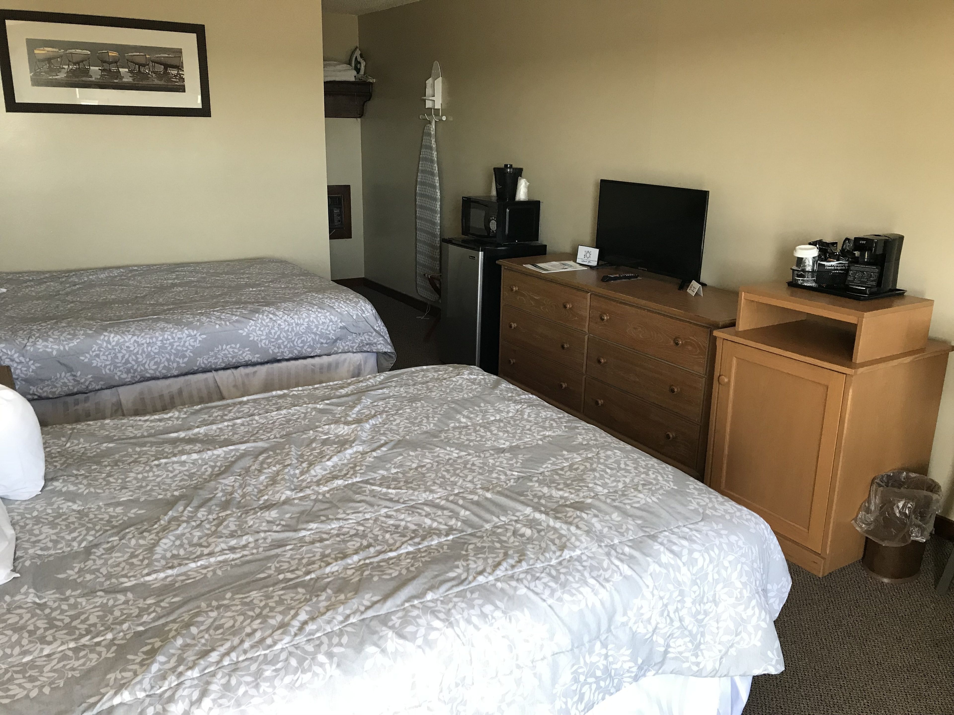 A hotel room with two beds, a dresser, a television, and a coffee maker.