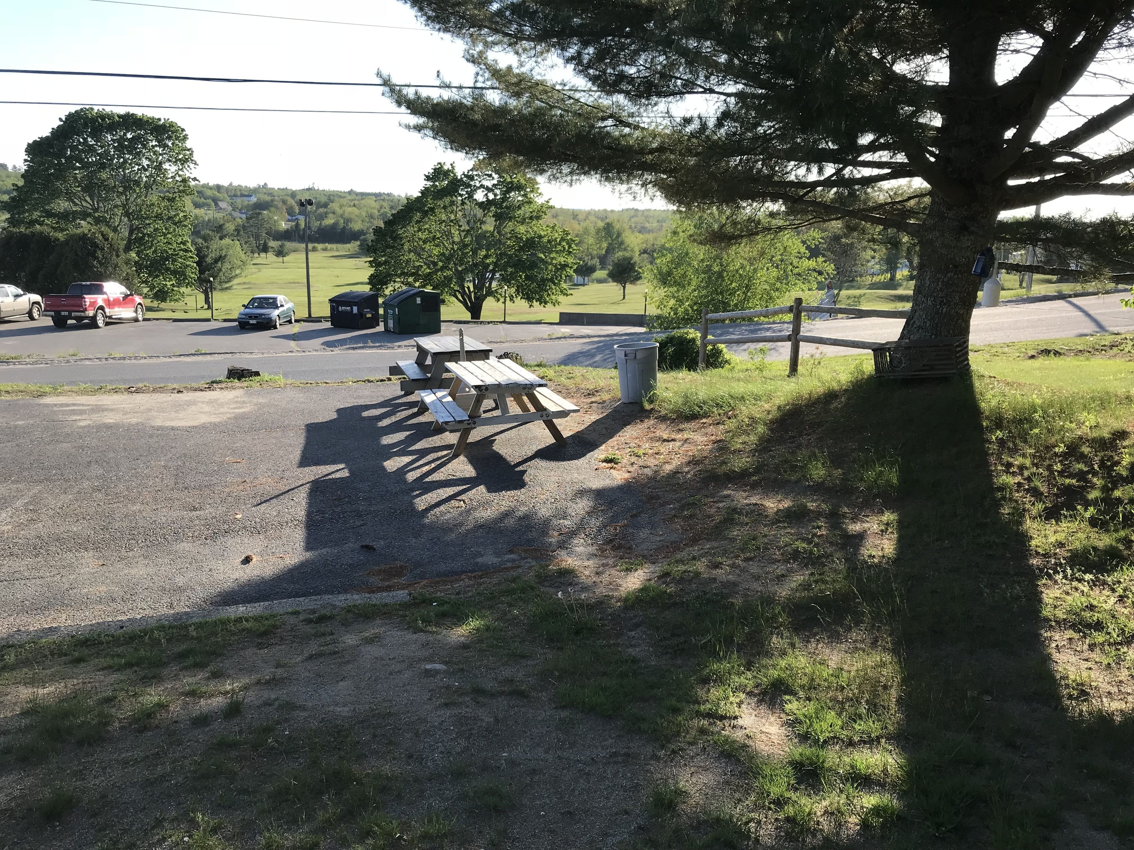 A picnic area with tables and benches, a trash bin, and a fence.