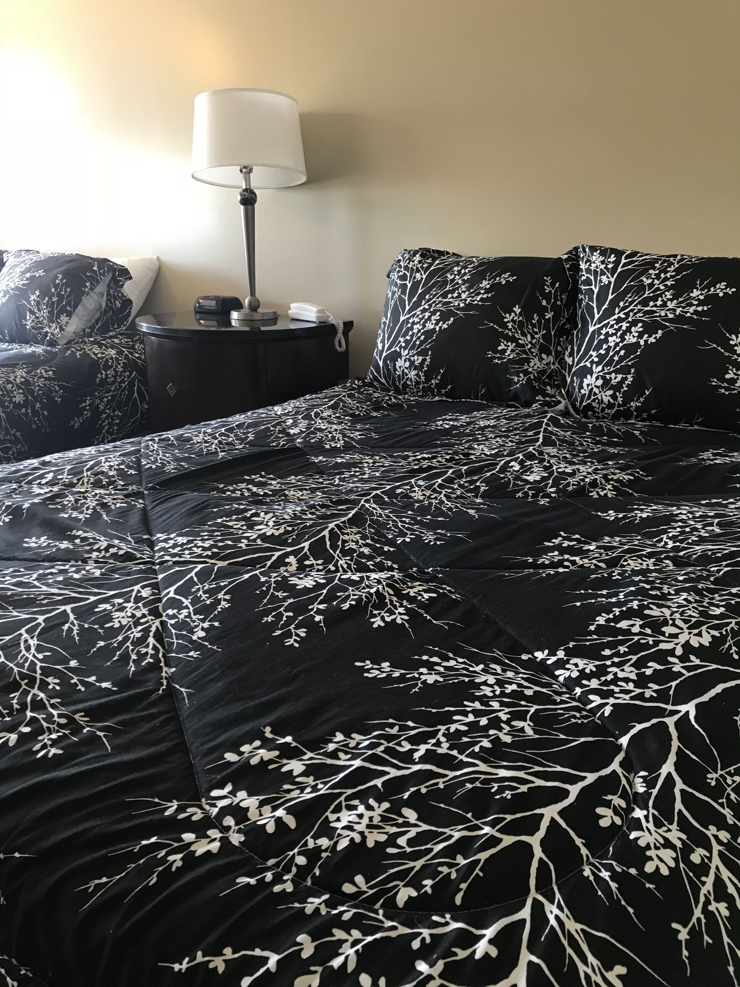 Un letto con una coperta a fiori bianco e nero, un comodino con una lampada e un telefono fissato al muro.