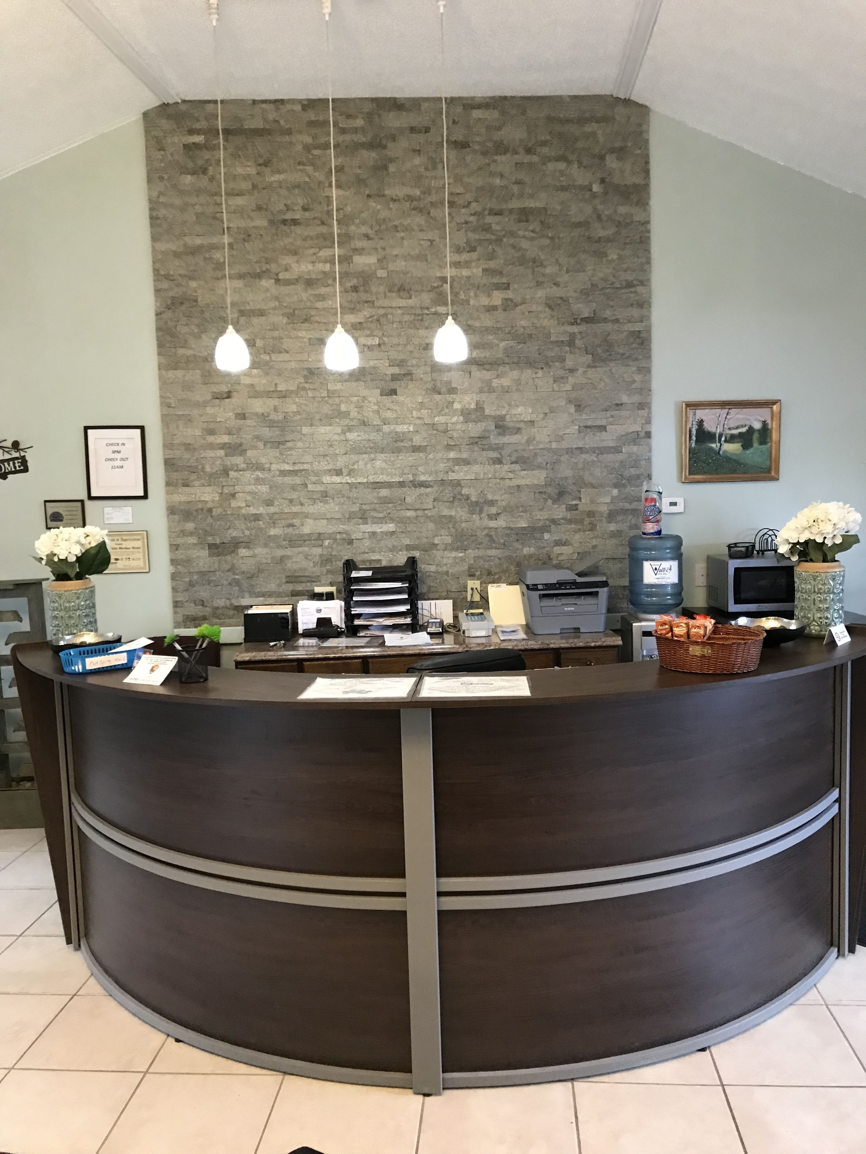 A reception desk with a dark wood finish, a stone wall behind it, and three pendant lights.