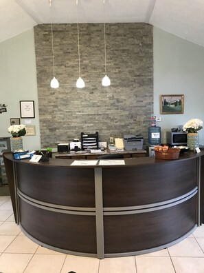 Una recepción con mostrador de madera oscura, pared de piedra y tres lámparas colgantes.