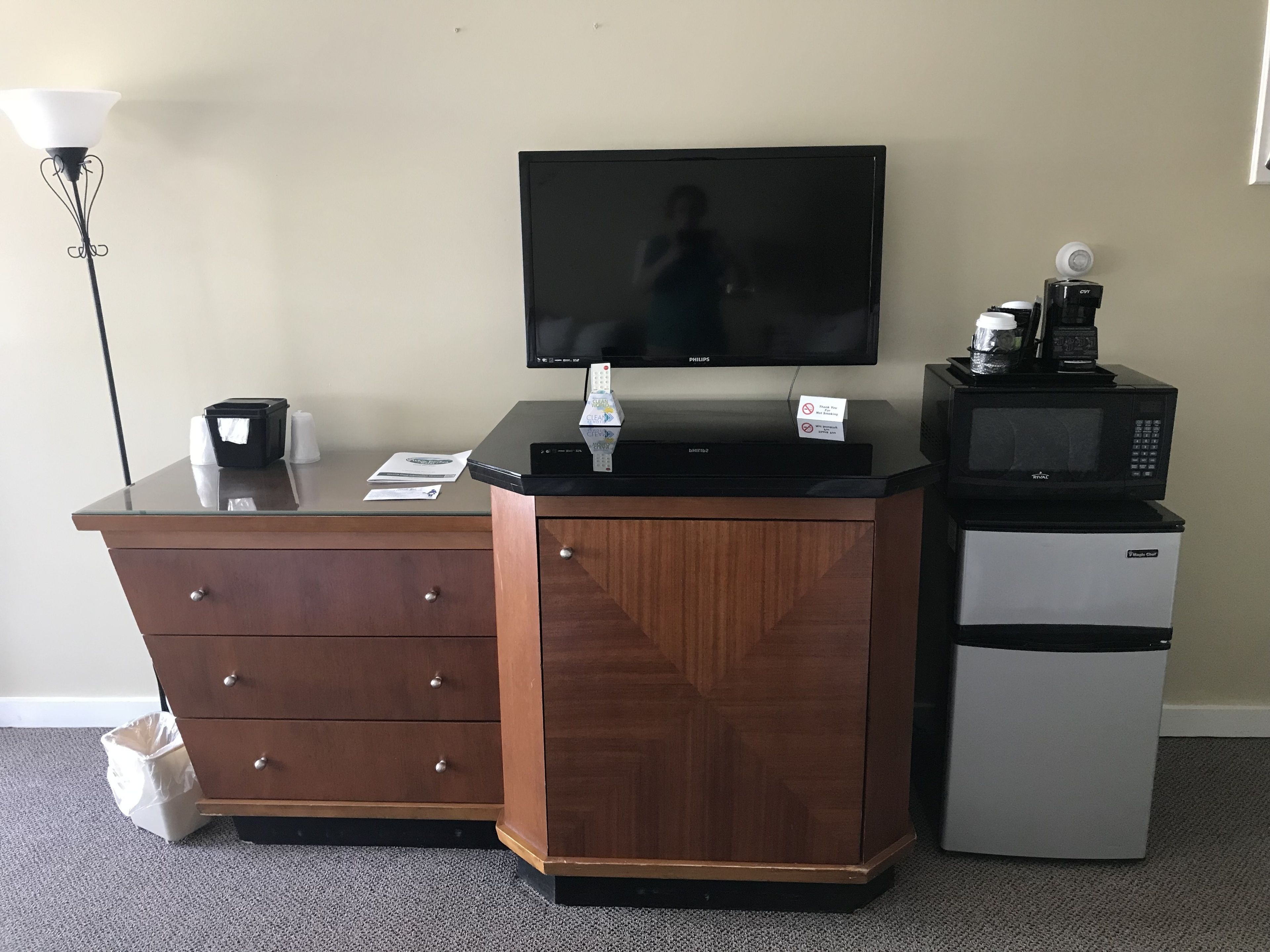 A hotel room with a wooden desk, a television, a coffee maker, and a refrigerator.