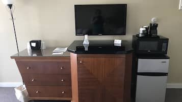 A hotel room with a wooden desk, a television, a coffee maker, and a refrigerator.