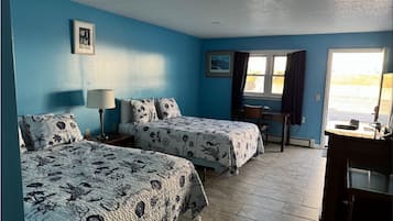 Quarto com duas camas, uma escrivaninha, uma cadeira, um abajur e uma janela com cortinas.