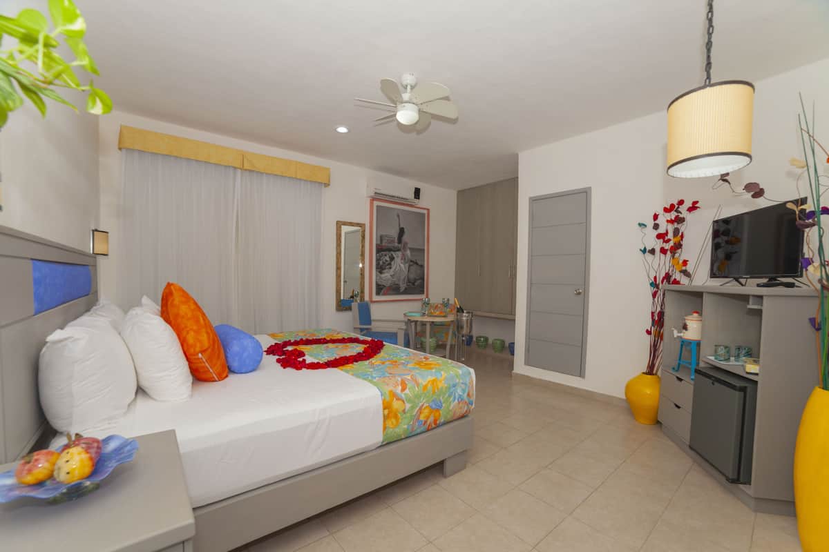 A hotel room with a bed, a desk, a chair, a TV, a ceiling fan, and a window with curtains.