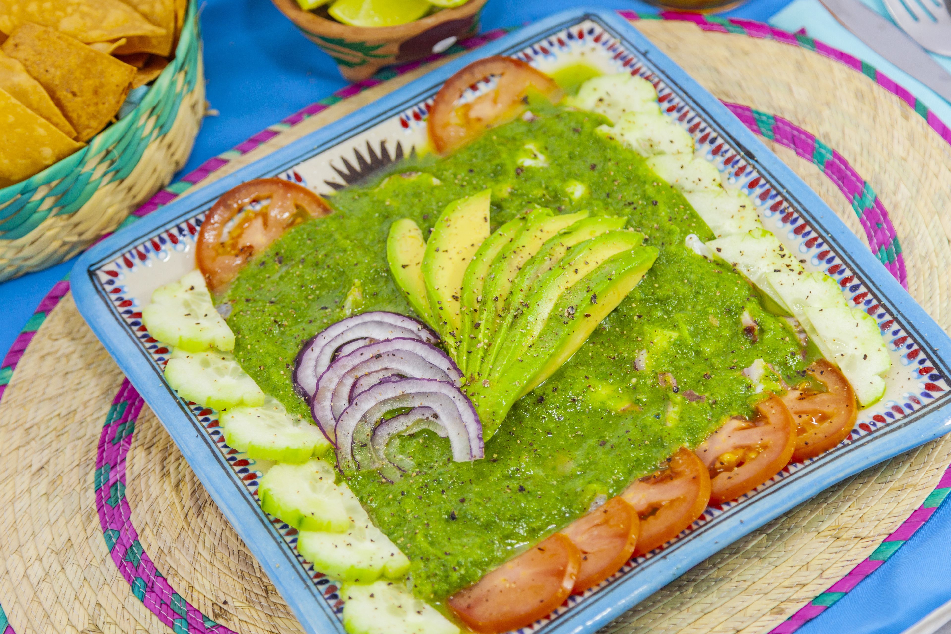 Un plato de guacamole con rodajas de aguacate, tomates y cebolla, sobre un plato azul y blanco estampado.