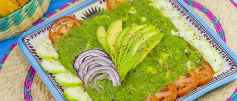 Un plato de guacamole con rodajas de aguacate, tomates y cebolla, sobre un plato azul y blanco estampado.